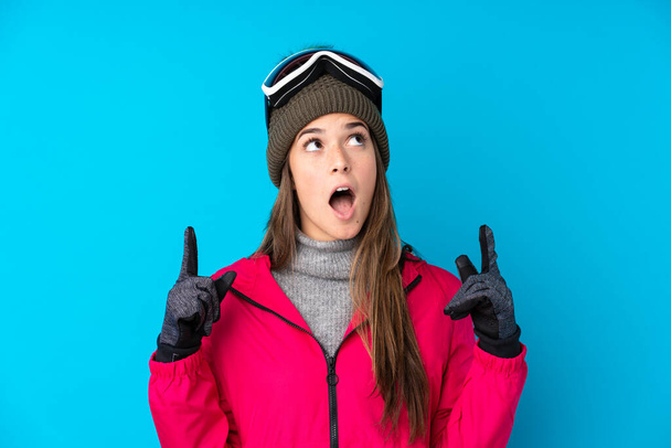 Teenager skier girl with snowboarding glasses over isolated blue background pointing with the index finger a great idea - Photo, image