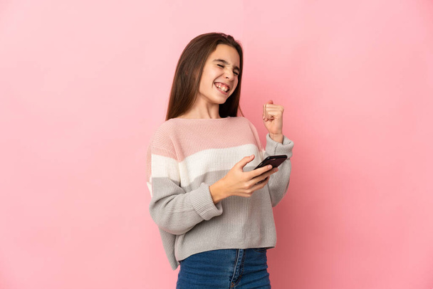 Kislány elszigetelt rózsaszín háttér telefon győzelmi pozícióban - Fotó, kép