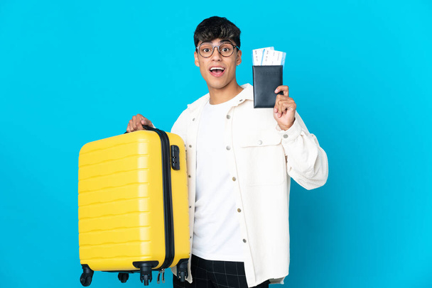 Νεαρός πάνω από απομονωμένο μπλε φόντο στις διακοπές με βαλίτσα και διαβατήριο - Φωτογραφία, εικόνα