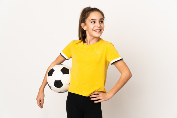 Маленькая девочка футболист изолирован на белом фоне позирует с руками на бедре и улыбается - Фото, изображение