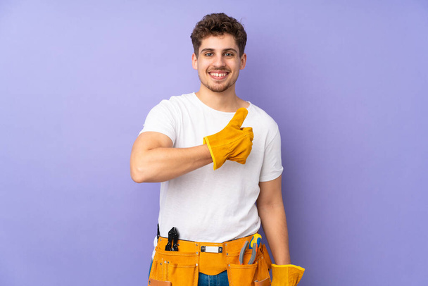Young electrician man over isolated on purple background giving a thumbs up gesture - Photo, Image