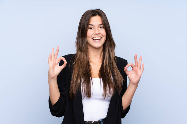 Νεαρή Βραζιλιάνα επιχειρηματίας πάνω από απομονωμένο μπλε φόντο δείχνει μια πινακίδα ok με τα δάχτυλα - Φωτογραφία, εικόνα