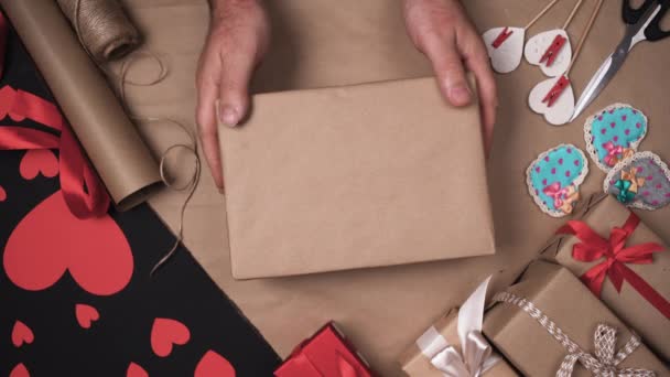 Männliche Hände auf dem Tisch mit Geschenken legen eine Schachtel in Bastelpapier gewickelt. legte einen großen Lichtbogen darauf. Valentinstag-Konzept. - Filmmaterial, Video