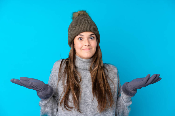 Menina adolescente com chapéu de inverno sobre fundo azul isolado com dúvidas com expressão facial confusa - Foto, Imagem