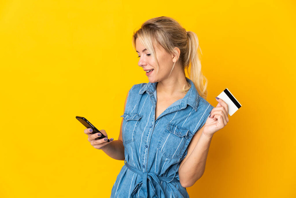 Молода російська жінка на жовтому тлі купує мобільний телефон з кредитною карткою. - Фото, зображення