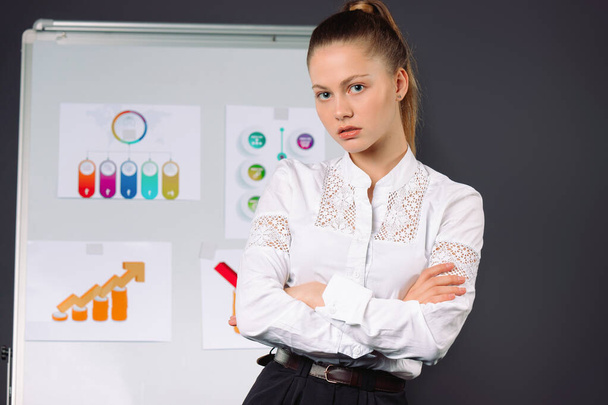 Serious businesswoman looking at the camera during a conference. Diagrams. Gray background. High quality photo - Foto, afbeelding