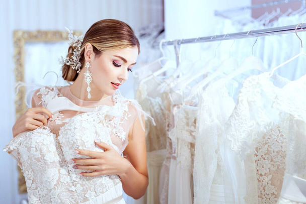 Młoda piękna kobieta wybiera sukienkę w salonie weselnym. - Zdjęcie, obraz