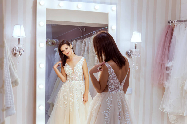 Młoda kobieta w sukni ślubnej stoi przed lustrem. - Zdjęcie, obraz
