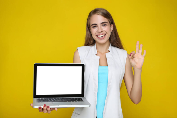 Mulher bonita segurando computador portátil e mostrando gesto OK no fundo amarelo - Foto, Imagem