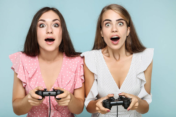 Young happy girlfriends playing computer game with joysticks on blue background - Foto, immagini