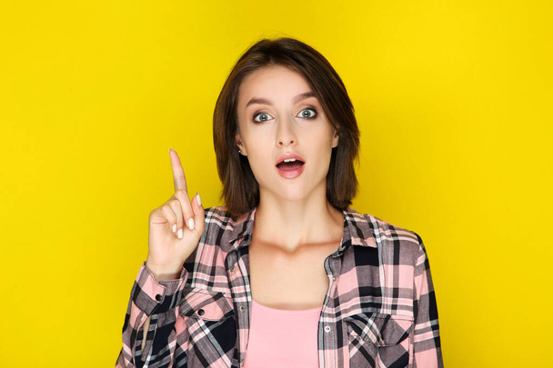 Surprised young woman pointing by finger on yellow background - Zdjęcie, obraz
