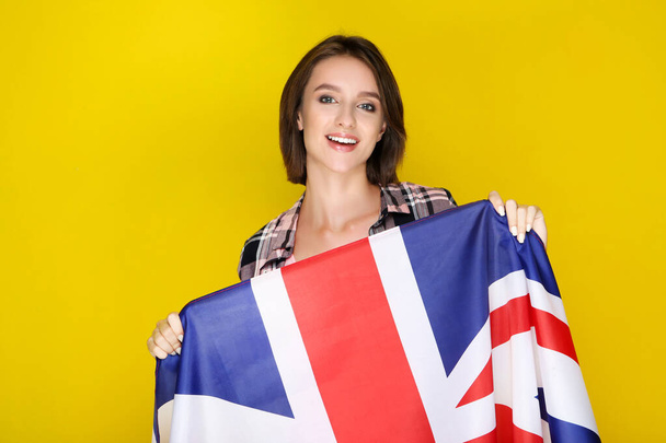 Beautiful young woman holding british flag on yellow background - Фото, изображение