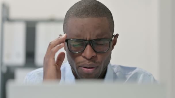 Primer plano del hombre africano que tiene dolor de cabeza mientras usa el ordenador portátil  - Imágenes, Vídeo