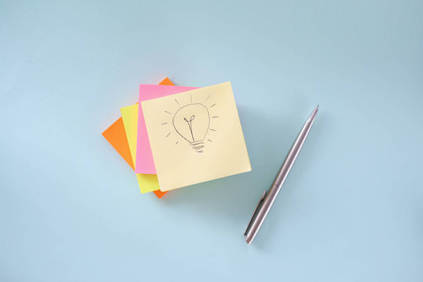 Лампочка рисует на листе бумаги. Многие красочные наклейки и шариковые ручки лежат на столе - Фото, изображение