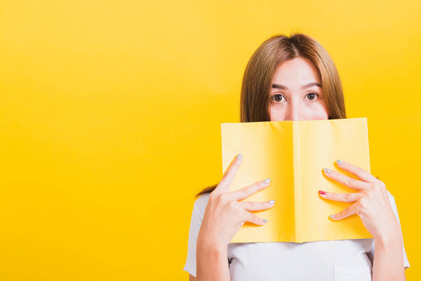 Portrait Asian Thai beautiful happy young lifestyle woman stands holding yellow book or diary her looking to camera, studio shot isolated on yellow background, with copy space - Foto, imagen