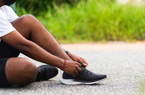 Close up Asian sport runner black man sitting shoelace trying running shoes getting ready for jogging and run at the outdoor street, health exercise workout concept - Zdjęcie, obraz