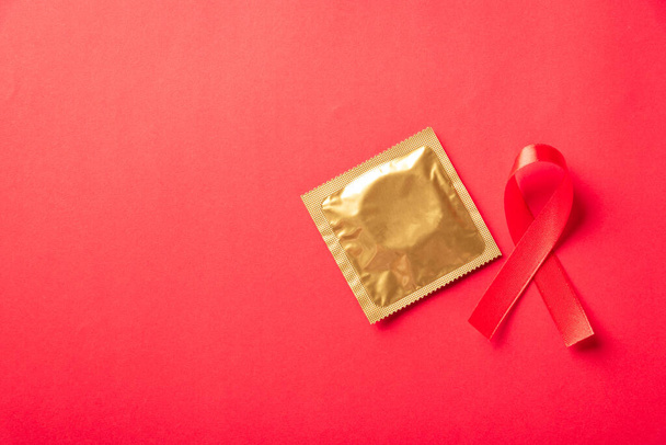 Red bow ribbon symbol HIV, AIDS cancer awareness and condom with shadows, studio shot isolated on red background, Healthcare medicine sexually concept, World AIDS Day - Photo, Image