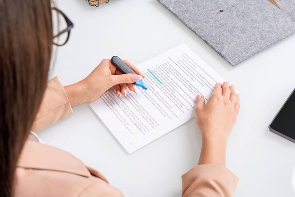 Молодая брюнетка деловая женщина подчеркивает основные моменты и условия контракта с синим маркером при чтении текста на рабочем месте - Фото, изображение