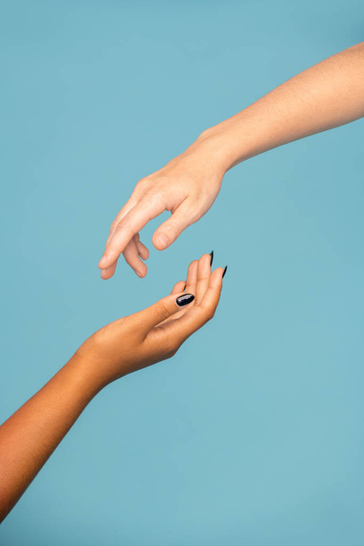 Χέρια νεαρών υποστηρικτικών γυναικών διαφορετικών εθνικοτήτων που τεντώνονται το ένα προς το άλλο για συμπάθεια σε μπλε φόντο - Φωτογραφία, εικόνα
