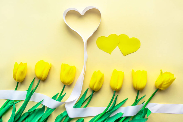 Słoneczny żółty kwiat. Żółte świeże tulipany z sercami na żółtym papierowym tle. Kartka okolicznościowa na Walentynki lub inne święta. Wybiórcze skupienie. Leżeć płasko. Przestrzeń kopiowania. - Zdjęcie, obraz
