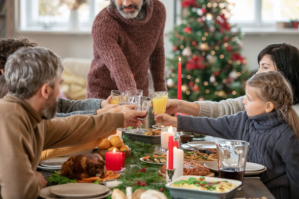 Deux couples et des filles mignonnes cliquetis avec des flûtes de jus d'orange sur la table de fête servi avec de la nourriture traditionnelle de Noël maison - Photo, image