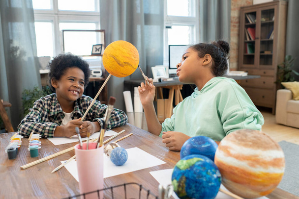 Дві чарівні змішані раси школярів в повсякденному житті малюють планети під час підготовки до уроку астрономії за столом в домашньому середовищі
 - Фото, зображення