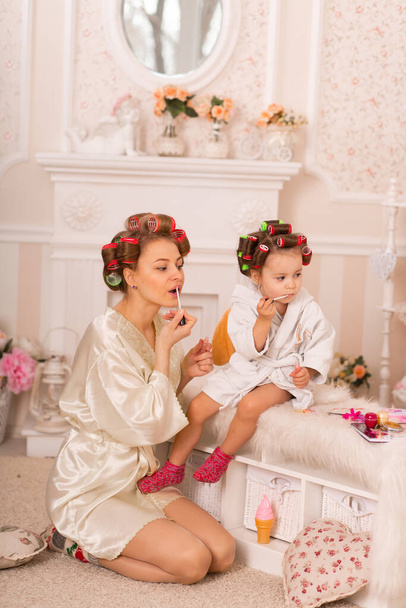 Adorable little girl with her mother in hair curlers apply makeup. Mom teaches daughter to use cosmetics. Beauty day. Girls are such girls. - Foto, Imagem