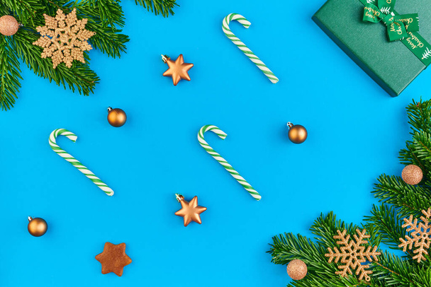 Flatlay of golden decorative snowflakes and balls on evergreen coniferous branches and giftbox surrounding sugar canes and toy stars - Photo, image