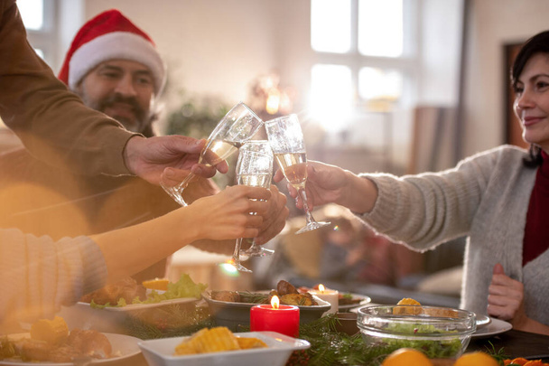 Kaksi pariskuntaa, joilla on huilut samppanjaa juhlapöydän päällä, tarjoillaan perinteisen joulun kotitekoisen ruoan kanssa paahtamalla lomaa varten. - Valokuva, kuva