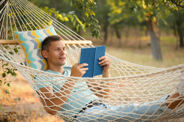 Man reading book in comfortable hammock at green garden - Valokuva, kuva