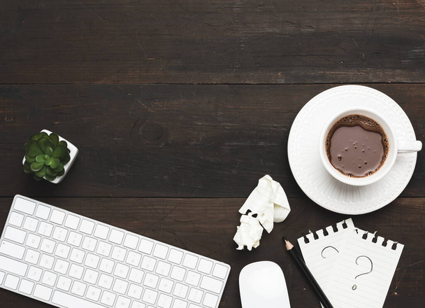 木製の茶色のテーブルの上に白いワイヤレスキーボードとマウスコーヒーと白いカップの横にトップビュー - 写真・画像