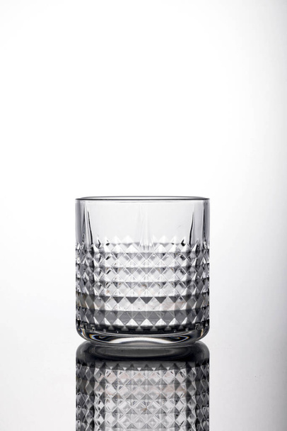 A shot of an empty whiskey glass with rhombus-shaped patterns on the white surface with a shadow - Φωτογραφία, εικόνα