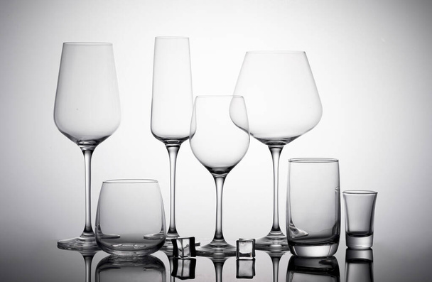 A glass set - empty wine glasses, champagne flute glass, vodka glass, whiskey glass, shot glass, highball glass on the white surface with shadows - Foto, Bild