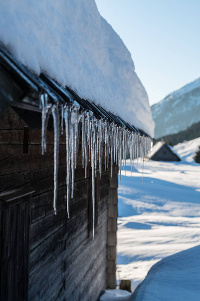 A vertical shot of icicles hanging from the edge of a roof - Fotoğraf, Görsel