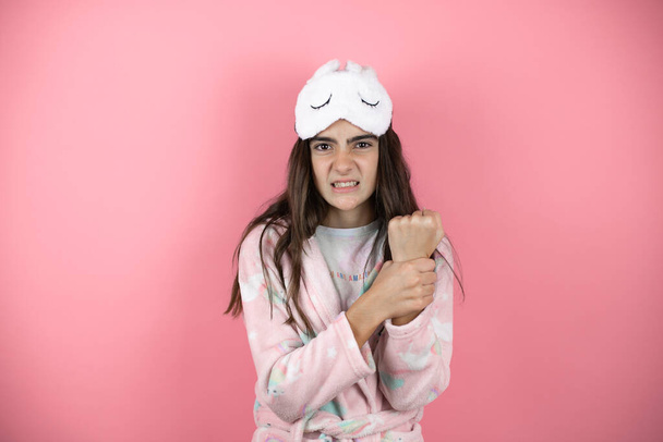Hezká dívka na sobě pyžamo a spánková maska přes růžové pozadí trpí bolestí na rukou a prstech, zánět artritidy - Fotografie, Obrázek