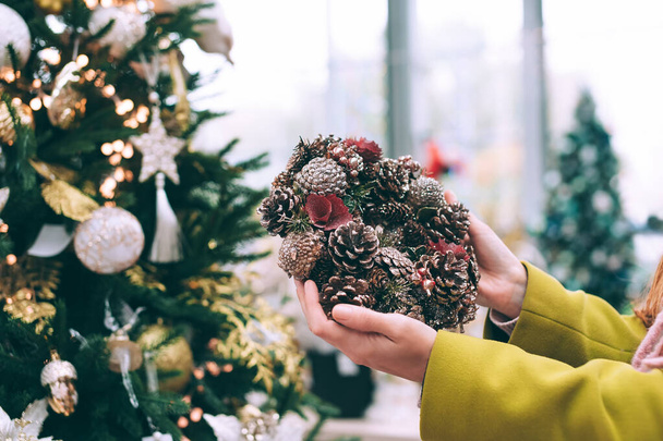 The girl is holding a New Year's wreath in her hands. Against the background of a Christmas tree in the store - Foto, imagen