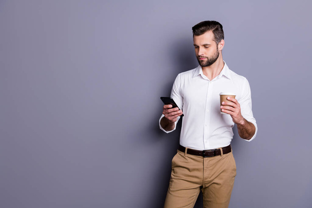 Portrait of his he nice attractive content classy imposing corporate focused brunet guy employer director using digital device reading news drinking latte isolated over gray pastel color background - Foto, Bild