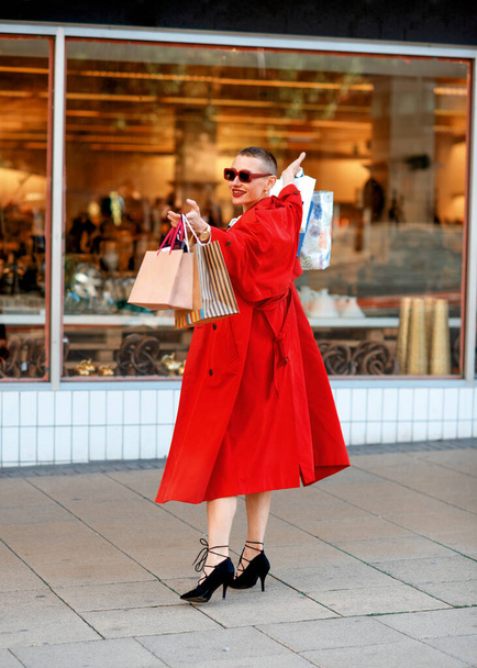femme heureuse en manteau rouge dansant dans la rue dans la ville après avoir fait du shopping - Photo, image