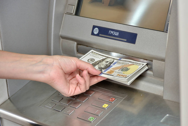 The girl's hand holds a bundle of dollar bills near the ATM. - Zdjęcie, obraz