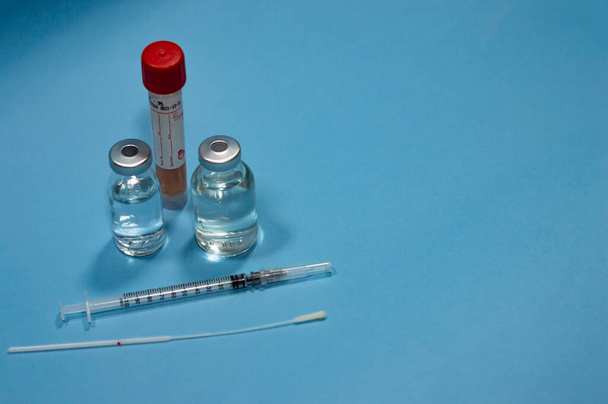 コロナウイルスに対する医療機器-空のコピースペース領域と青の背景にワクチンとタンポン、注射器とcovidテスト - 写真・画像