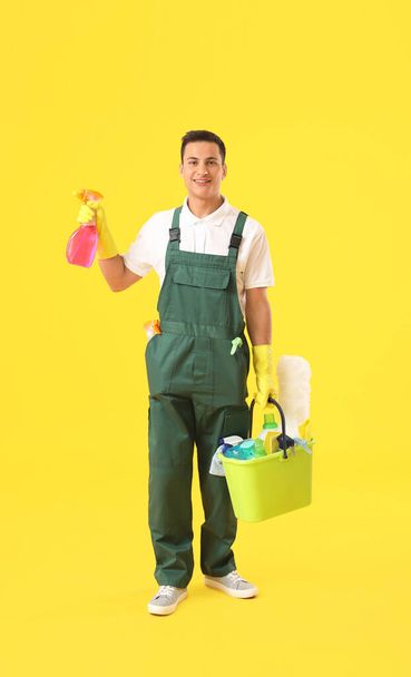 Fiatal férfi gondnok tisztítószerek színes háttér - Fotó, kép