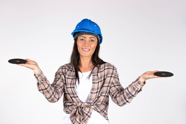 A brunette in a hard hat with her arms outstretched smiles and poses with abrasive flap disc and cutting abrasive disc for angle grinder.. White background. High quality photo - 写真・画像