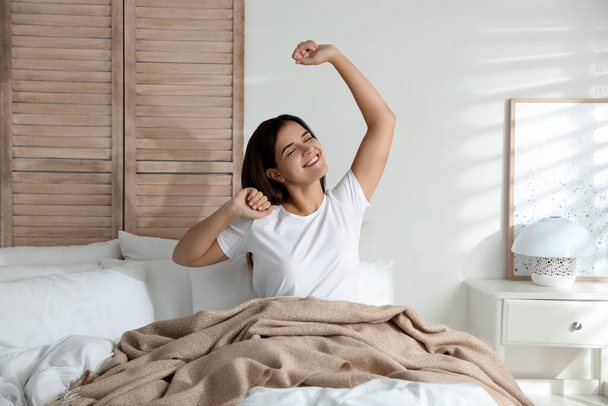 Woman covered with warm beige plaid stretching on bed indoors - Photo, image