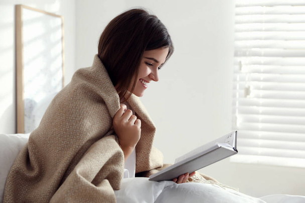 Woman with warm beige plaid reading book in bedroom - Zdjęcie, obraz