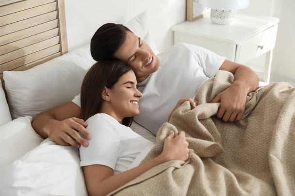 Happy couple covered with warm beige plaid sleeping in bed indoors - Foto, Imagen