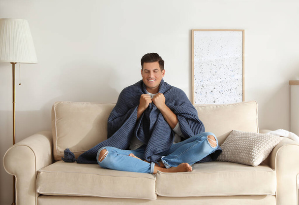 Man covered with warm dark blue plaid sitting on sofa at home - Zdjęcie, obraz