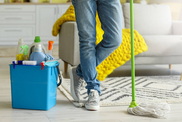 Young man with cleaning supplies at home - Фото, изображение