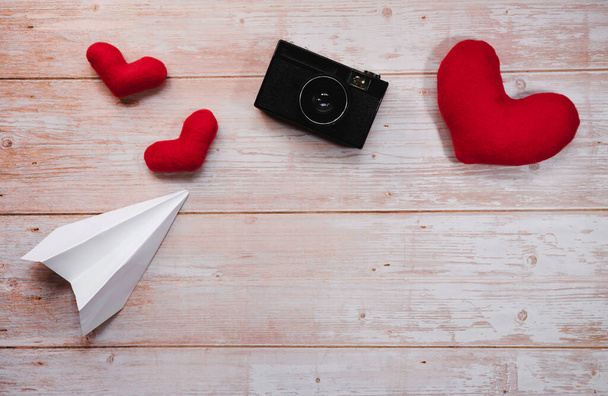 Λευκό origami χάρτινο αεροπλάνο, κόκκινο γεμιστό βελούδινες καρδιές παιχνιδιών, και μαύρο παλιό ρετρό φωτογραφική μηχανή ταινία. Ξύλινο επίπεδο φόντο θέσει για τις διακοπές Ημέρα του Αγίου Βαλεντίνου στις 14 Φεβρουαρίου. - Φωτογραφία, εικόνα