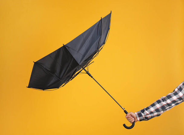 Man holding umbrella caught in gust of wind on yellow background, closeup - 写真・画像