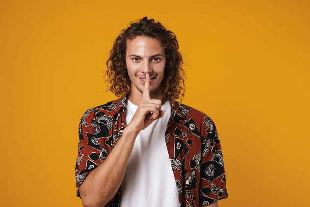 Photo of pleased handsome guy smiling and showing silence sign isolated over yellow background - Foto, Bild
